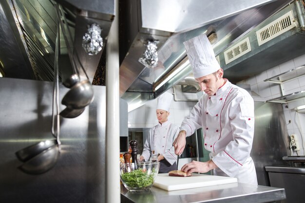 Zdjęcie szef kuchni krojenia mięsa na desce do krojenia, profesjonalny kucharz trzyma nóż i krojenia mięsa w restauracji