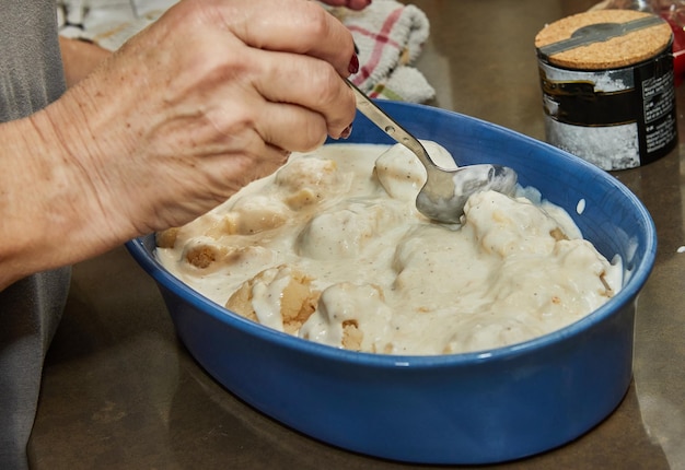 Szef kuchni nalewa kalafior sosem beszamelowym do naczynia ceramicznego do pieczenia w piekarniku