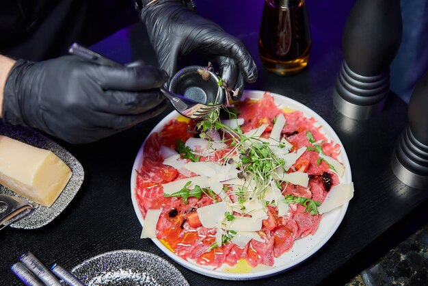 Szef kuchni przygotowuje carpaccio z cielęciny z rukolą i parmezanem na oczach Gości restauracji