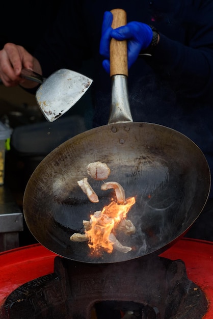 Szef kuchni przygotowuje chińskie jedzenie na ulicznym festiwalu żywności Sfotografowany, gdy jedzenie przelatuje nad patelnią wypełnioną ogniem i dymem
