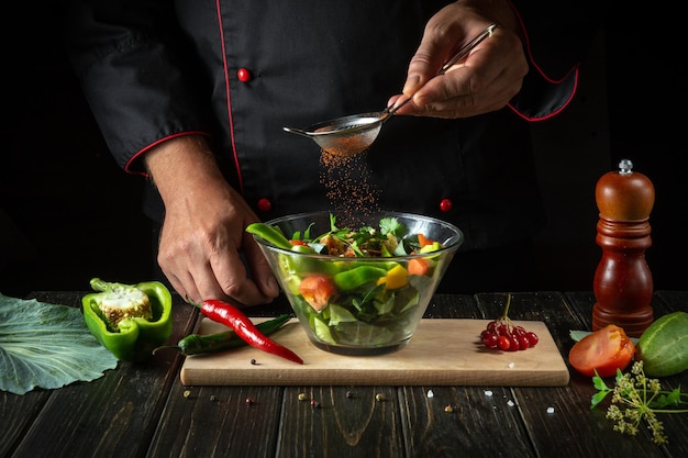 Szef kuchni przygotowuje dania wegetariańskie ze świeżych warzyw Koncepcja menu dla hotelu na ciemnym tle