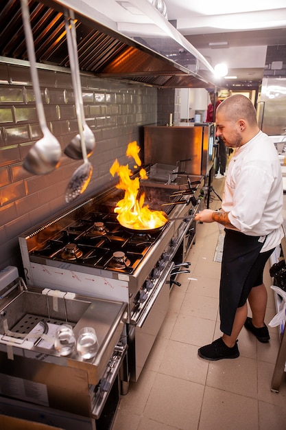 Szef kuchni przygotowuje danie na kuchence z otwartym ogniem w kuchni restauracji.