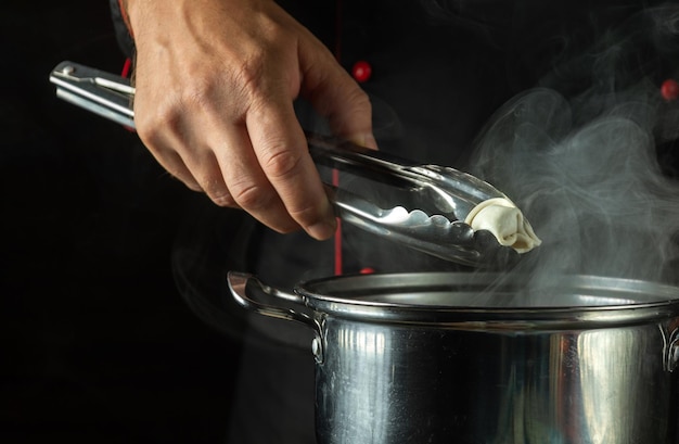 Szef kuchni przygotowuje knedle w kuchni w garnku Koncepcja pysznego obiadu na ciemnym tle Narzędzie kuchenne w ręku kucharza