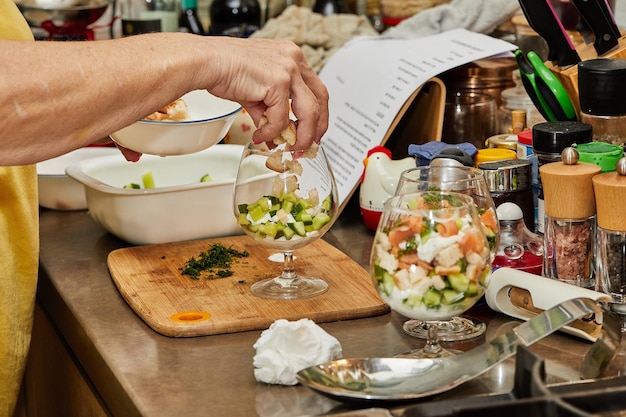 Szef kuchni robi letnią sałatkę w szklance z łososiem, ogórkami, grzankami, ziołami i świeżą śmietaną. Eleganckie letnie połączenie