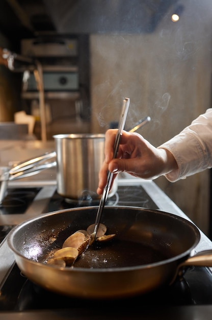 Szef kuchni smażący małże w komercyjnej kuchni w restauracji zbliżenie na rękach