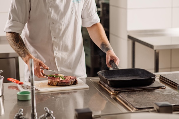 Szef kuchni smaży stek na patelni w kuchni restauracji