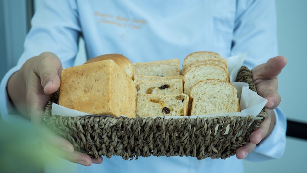 Szef kuchni trzyma kosz wiklinowy wewnątrz chleba domowej roboty dwiema rękami.