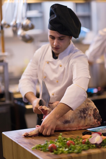 szef kuchni używający siekiery podczas krojenia dużego kawałka wołowiny na drewnianej desce w kuchni restauracji