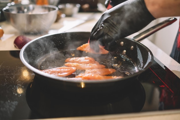 Szef kuchni w czarnych gumowych rękawiczkach smaży pomidory na patelni
