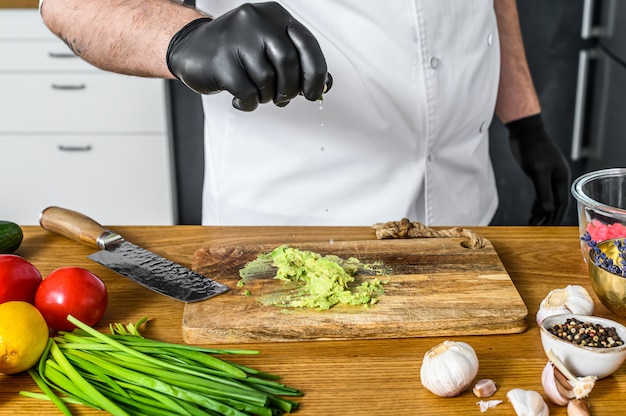 Zdjęcie szef kuchni w czarnych rękawiczkach przygotowuje guacamole ze świeżego awakado.