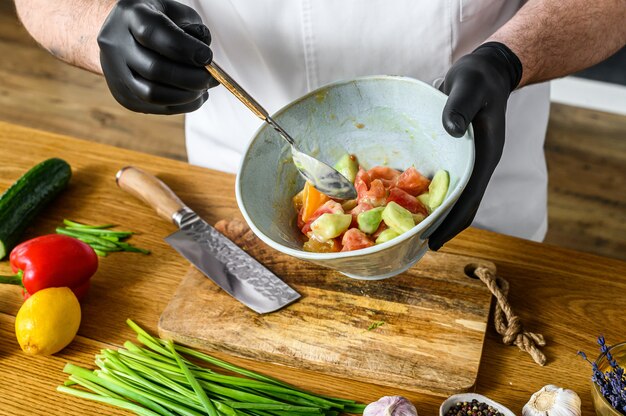 Szef kuchni w czarnych rękawiczkach przygotowuje wegetariańską sałatkę warzywną.