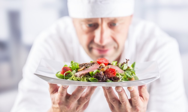 Szef kuchni w kuchni hotelu lub restauracji trzymając talerz z jedzeniem przed podaniem.