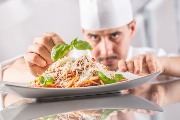 Szef kuchni w kuchni restauracji przygotowuje i dekoruje posiłki rękami. Gotuj przygotowując spaghetti bolognese.