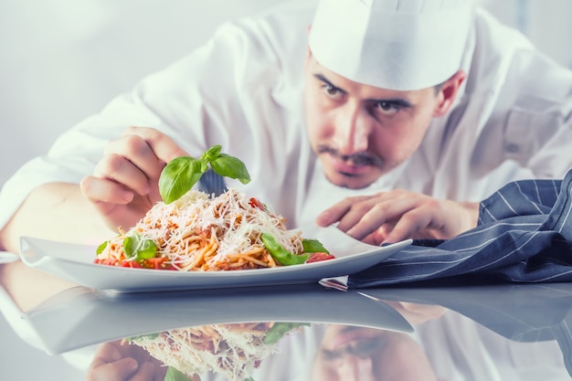 Szef kuchni w kuchni restauracji przygotowuje i dekoruje posiłki rękami. Gotuj przygotowując spaghetti bolognese.