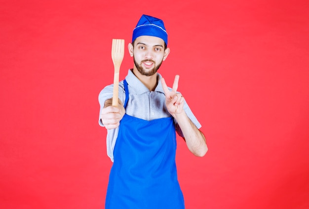 Szef kuchni w niebieskim fartuchu trzymający drewnianą łopatkę i mający dobry pomysł.