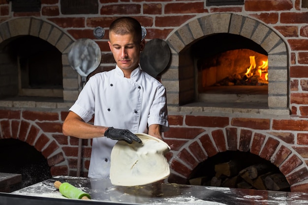 Szef pizzy rzucający ciasto na pizzę w powietrzu w tradycyjnej kuchni pizzerii