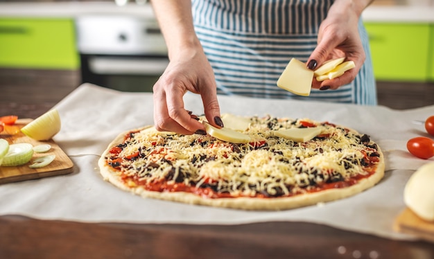 Szefowa kuchni w fartuchu kładzie ser mozzarella na surowej pizzy