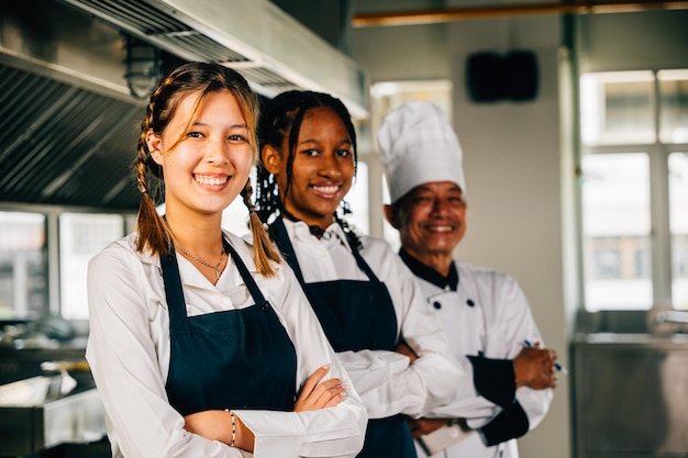 Szefowie kuchni w mundurach uśmiechają się do kamery w profesjonalnej kuchni, ilustrując wiedzę, pracę zespołową i jedność, nauczanie i uczenie się w akcji.