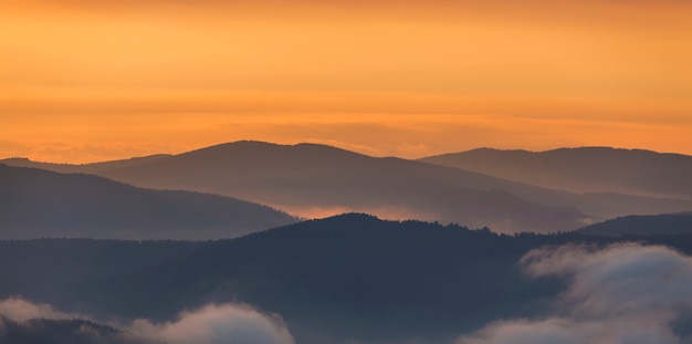 Szeroka panorama mgłowych gór o zachodzie słońca na jasnej jasnej pomarańczowej przestrzeni kosmicznej kopii