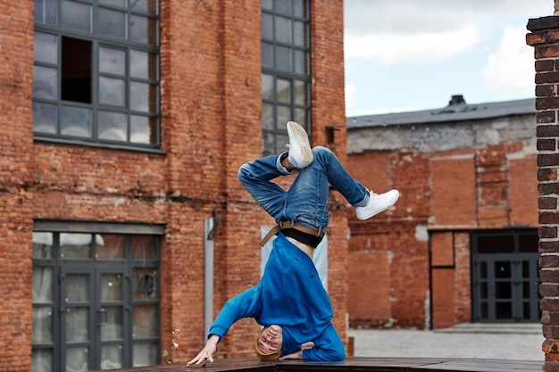 Szeroki kąt ujęcia młodego mężczyzny robi pozę breakdance na rękach w miejskim otoczeniu fabrycznym