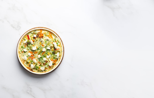 Szeroki transparent jajko frittata omlet z sezonowymi warzywami i serem w talerzu na białym tle marmuru Zdrowa dieta jedzenie koncepcja widok z góry z miejscem na tekst