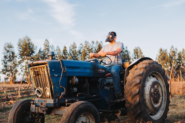 Szerokie ujęcie rolnika z maską zarazy podczas jazdy starym traktorem na swoim polu uprawnym