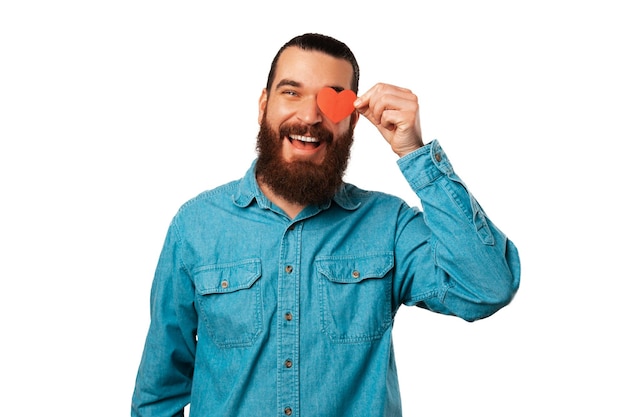 Szeroko uśmiechnięty brodaty mężczyzna trzyma nad okiem papier w kształcie serca
