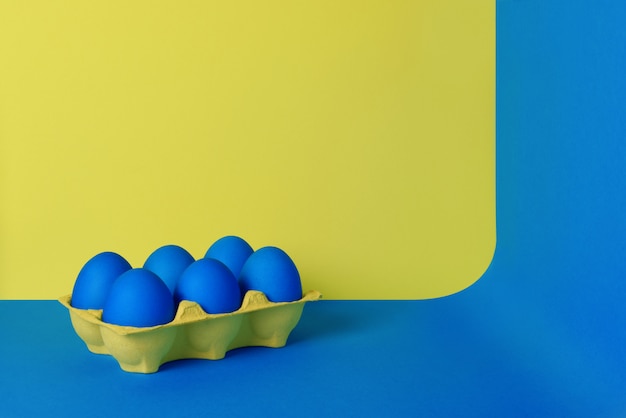 Zdjęcie sześć błękitnych malujących wielkanocnych jajek w żółtym opakowaniu na błękitnym i żółtym tle