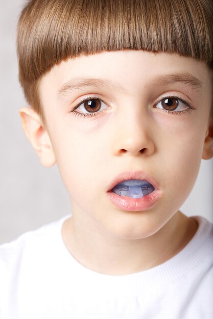 Sześcioletni chłopiec pokazuje miofunkcyjny trener, aby oświetlić nawyk oddychania przez usta. Zbliżenie