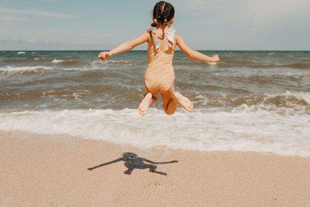 Sześcioletnia dziewczyna w żółtym stroju kąpielowym na plaży ludzi od tyłu