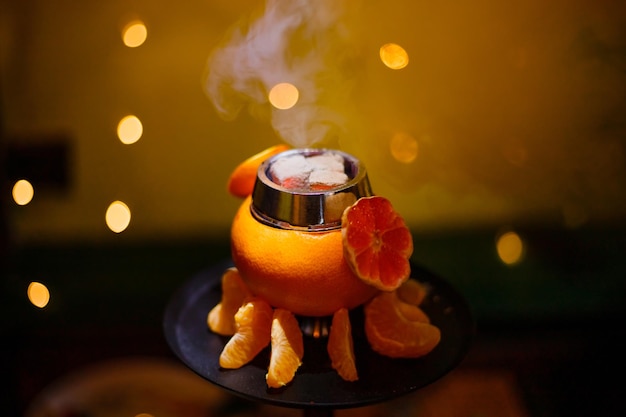 Zdjęcie szisza na pomarańczy z dymem, z plasterkami mandarynki. wysokiej jakości zdjęcie. zdjęcie z bliska