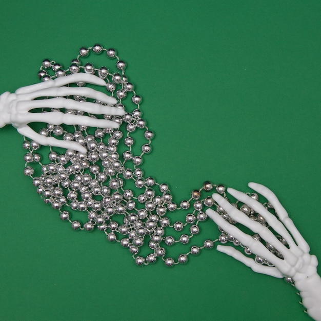 Szkielet dłoni podtrzymywany jest przez ozdobną perłową wstążkę na zielonym tle. Minimalistyczna koncepcja płaskiego układania.