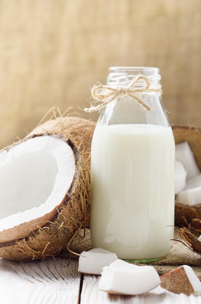 Szklana butelka mleka lub jogurtu na konopnej serwetce na białym drewnianym stole z kokosem na bok