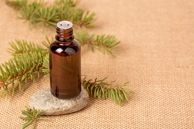 Szklana butelka z aromatycznym olejkiem lub serum na kamieniu i gałązką sosnowych igieł. Koncepcja spa naturalnych organicznych kosmetyków. Na tle płótna.