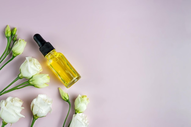Szklana butelka z olejkami kosmetycznymi z wiosennymi kwiatami eustoma Butelki z serum lub olejkiem eterycznym na różowym tle Produkty kosmetyczne