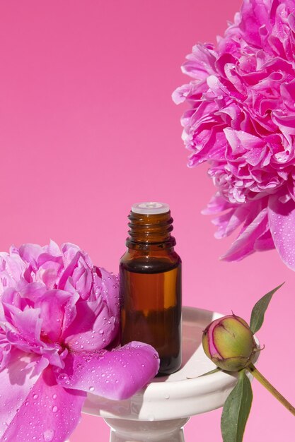 Szklana butelka z olejkiem eterycznym na podium na różowym tle z kwiatami piwonii