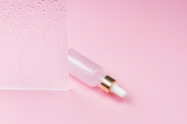 Szklana butelka z zakraplaczem olejku do pielęgnacji skóry na różowym tle Nawilżające serum witaminowe do skóry twarzy Estetyczny minimalizm