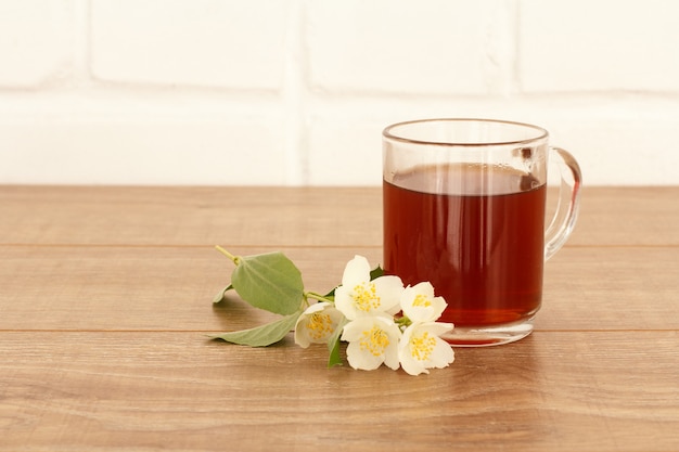 Szklana filiżanka herbaty z białymi kwiatami jaśminu na drewnianym pulpicie.