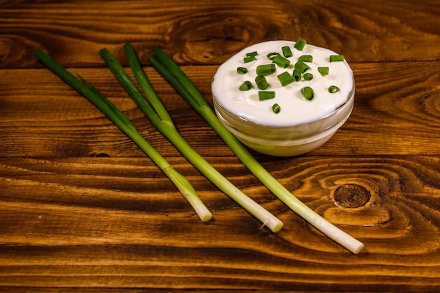 Szklana miska z kwaśną śmietaną i zieloną cebulą na drewnianym stole