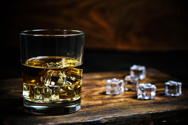 Szklana schłodzona whisky z kostkami lodu na drewnianym tle w piwnicy.