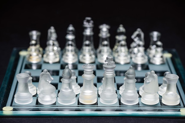 Szklane przezroczyste szachy na szachownicy selektywnej ostrości zbliżenie izolowane na czarno