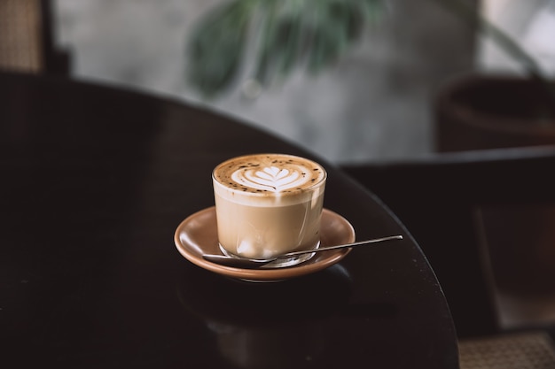 Szklanka cappuccino z latte art na spodku i łyżką na czarnym stole. Napój śniadaniowy