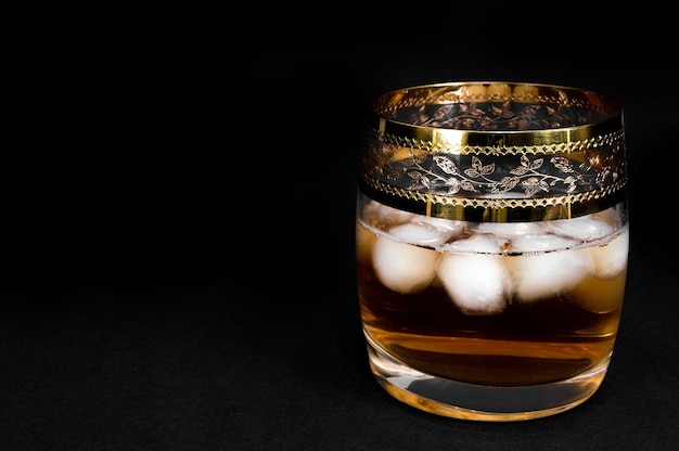 Zdjęcie szklanka ciemnoczerwonej whisky lub xabourbon z lodem na czarnym tle zbliżenie zdjęcie alkoholu