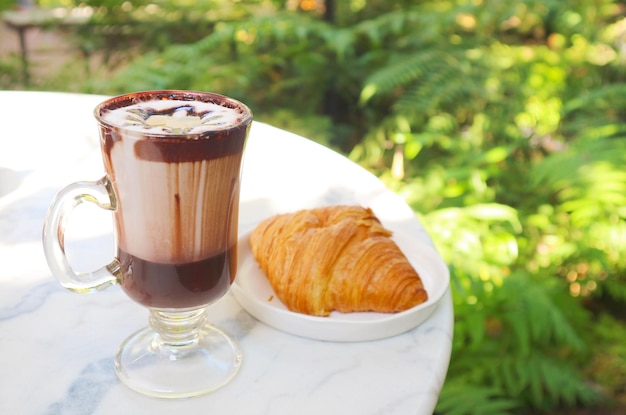 Szklanka gorącej czekolady z francuskim rogalikiem na białym stole