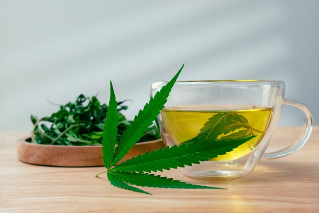 Szklanka gorącej herbaty marihuany na drewnianym stole. Herbata ziołowa z konopi z suszonymi liśćmi.