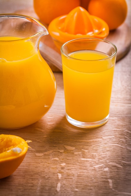 Szklanka i dzbanek soku i pomarańczy z sokowirówką na drewnianym stole