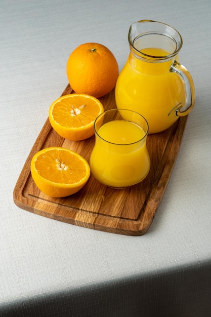 Szklanka i dzbanek soku pomarańczowego na drewnianym stojaku pokrojone w pomarańczowe lniane tło