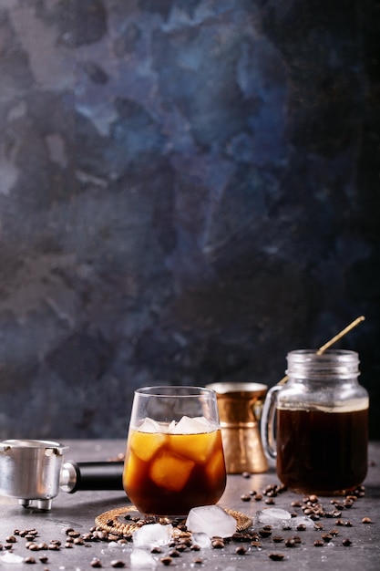 Zdjęcie szklanka kawy mrożonej z kostkami lodu podana ze śmietaną, miedzianym cezve i ziarnami kawy na ciemnej ścianie