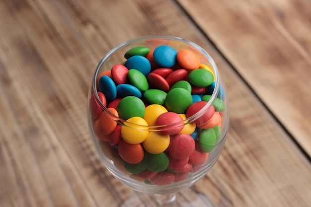 Szklanka kolorowych cukierków m & m stoi na drewnianym stole.