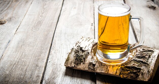 Szklanka lekkiego piwa na brzozowej podstawce na drewnianym stole